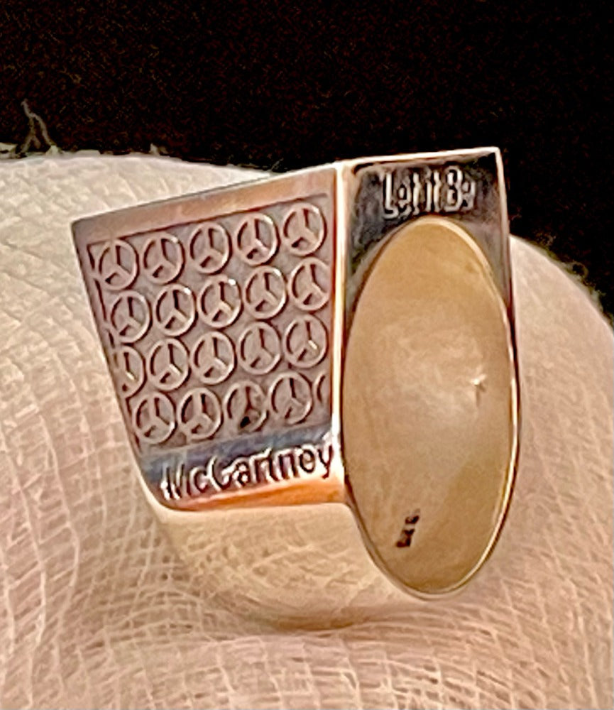 Serling silver ring with Guitar tab feature on the top showing the chord progression for the song Let it Be  (C,G,Am,F) The words Let it Be on the sides. The letters are in black. The shoulders of the ring show black peace signs and the words Lennon and McCartney below the peace signs